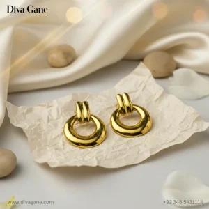 gold-finished earring. The earring features a thick, polished circular hoop suspended from a double-bar gold post. The background is a dark emerald green silk with warm, out-of-focus golden bokeh lights, creating a luxury aestheticots