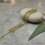 About Close-up of a girl's hand with dark red nail polish holding a pink drink, wearing a cascading gold multi-chain bracelet at a festive event