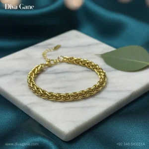 Top-down view of a gold woven link bracelet placed on a white marble square with a green leaf accent and bokeh fairy lights