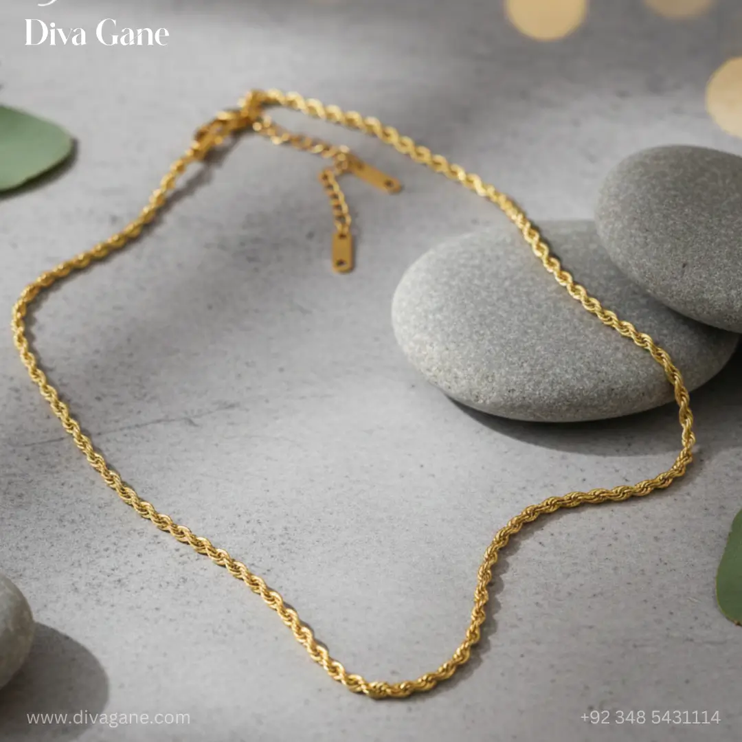 luxe minimalist flat link chain Professional jewelry photography of a gold twisted rope chain displayed on smooth grey river stones with soft eucalyptus leaves and bokeh lighting