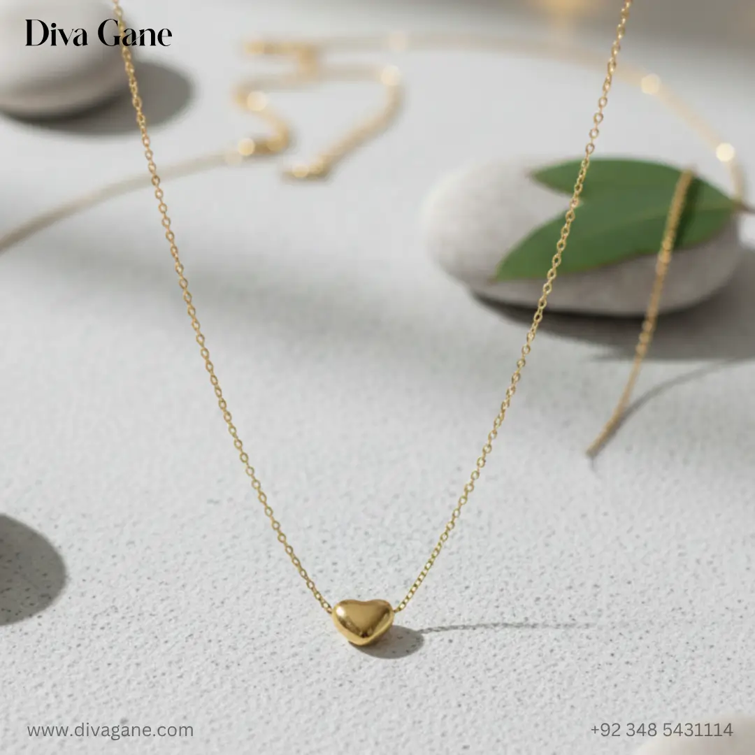 the amora minimalist 3d gold heart charm A macro photograph of a small, polished 3D gold heart pendant on a fine gold chain, resting on a textured white surface with soft bokeh lights