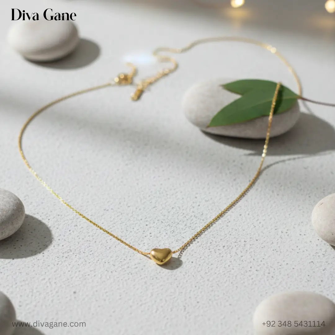 the amora minimalist 3d gold heart charm Dainty gold heart necklace displayed artistically on smooth white river stones with a single green leaf and warm background lighting