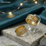 About A wide 18K gold plated triple-band ring with pavé crystal rows resting on a gray stone pedestal with green velvet and fairy lights