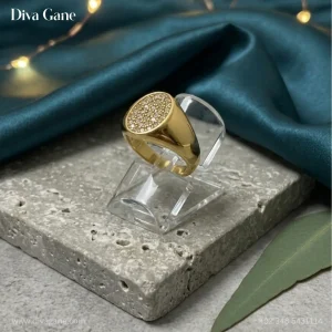 Luxury 18K gold plated oval signet ring with pavé crystal center resting on a dark teal silk cloth background