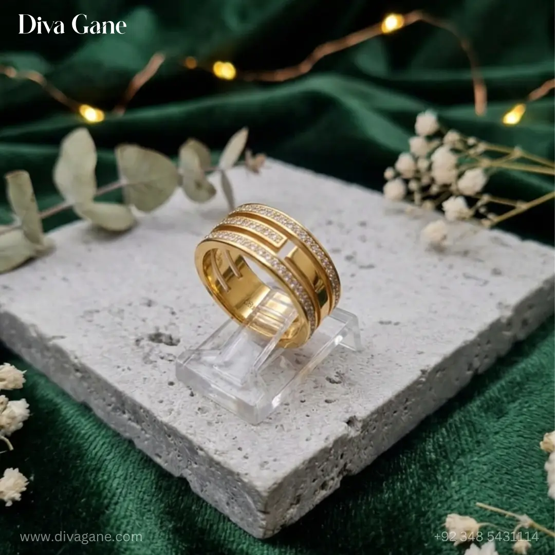 luxe 18k gold plated triple layer pavé statement ring A wide 18K gold plated triple-band ring with pavé crystal rows resting on a gray stone pedestal with green velvet and fairy lights